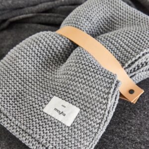 coperta in misto lana lavorata a maglia di colore grigio piegata e chiusa con un cinturino in pelle naturale