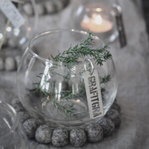 piccola vasi a boccia di vetro con supporto in feltro ad anello di palline di lana color grigio con rametto di verde come decorazione