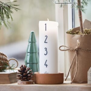candela dell'avvento in cera bianca numerata da 1 a 4 sul davanzale di una finestra insieme ad altre decorazioni natalizie