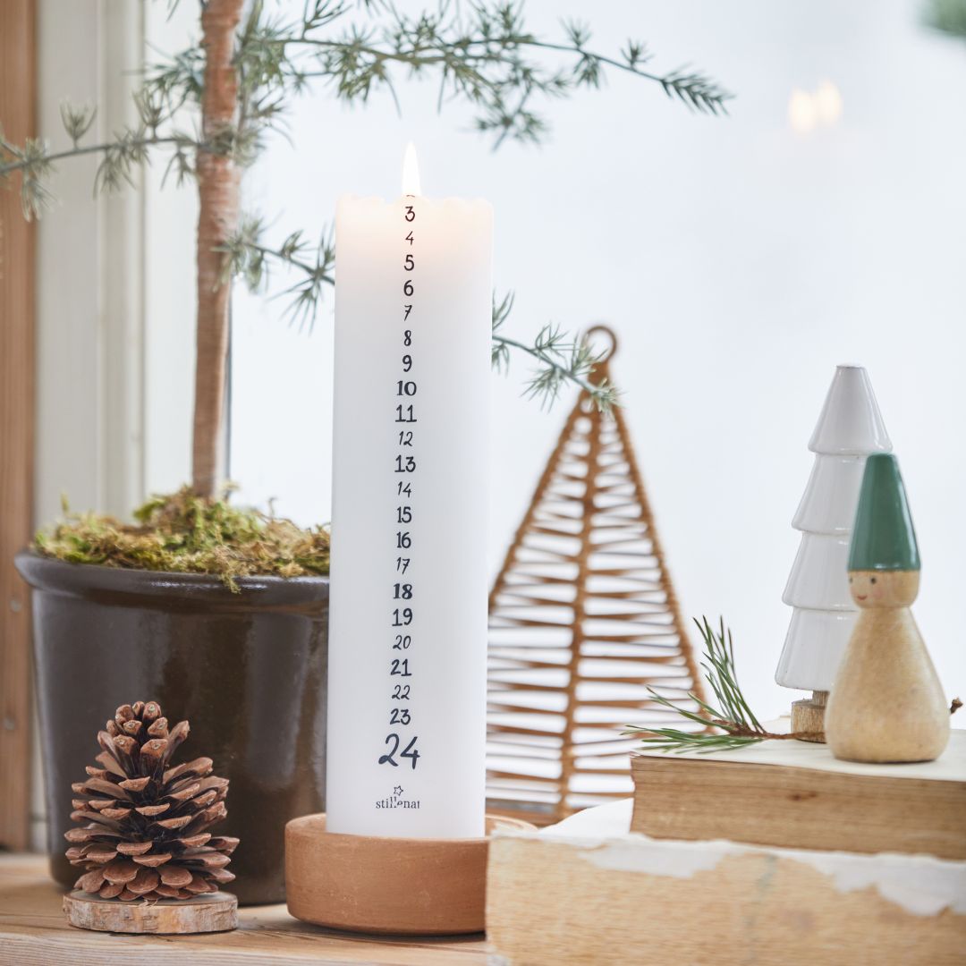 candela dell'avvento numerata da 1 a 24 in cera bianca su un davanzale insieme ad altre decorazioni natalizie