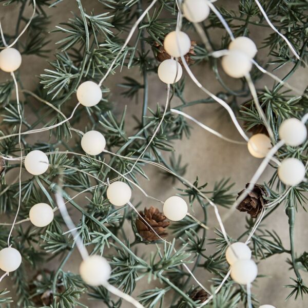 filo di luci natalizie a forma di pallina di neve su un ramo di cedro
