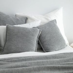 copricuscini in maglia di lana a trama grossa color grigio chiaro di misura 50x50 utilizzati su un letto con altri cuscini e coperta sempre in lana grigia