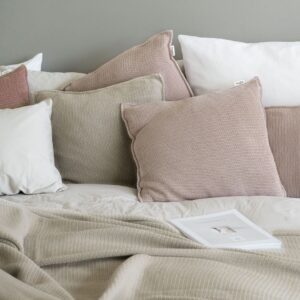 copricuscini lavorati a maglia con filato a trama grossa color rosa cipria di misura 50x50 utilizzati su un letto con altri cuscini e coperte
