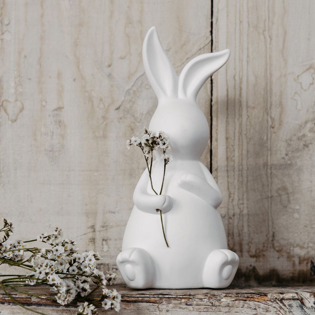 decorazione pasquale a forma di coniglietto in ceramica bianca opata con un decoro floreale nella mano destra appoggiato su una mensola