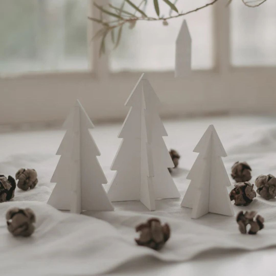 paesaggio natalizio con tre alberelli di natale in legno smaltato bianco sul davanzale della finestra e decorati con delle pigne