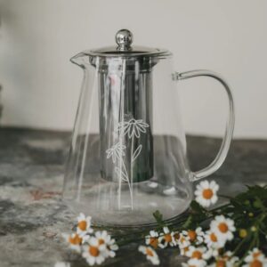 teiera di design in vetro borosilicato trasparente e filtro con coperchio in acciaio inossidabile, sul fronte della teiera c'è un'elegante stampa in bianco di due margherite stilizzate