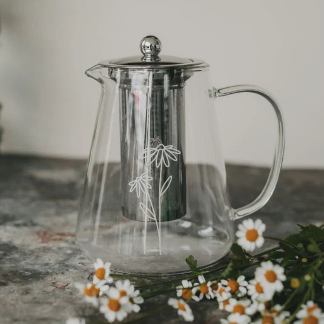 teiera di design in vetro borosilicato trasparente e filtro con coperchio in acciaio inossidabile, sul fronte della teiera c'è un'elegante stampa in bianco di due margherite stilizzate